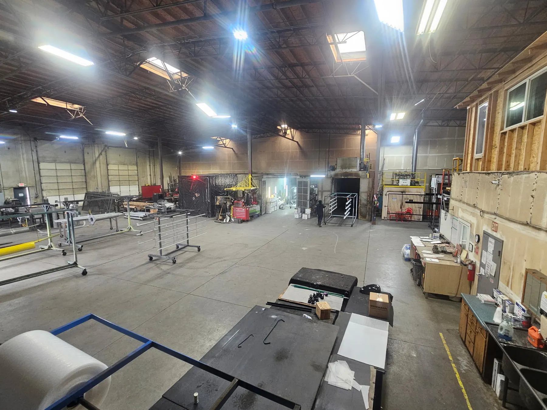 Wide view of Secoma Powder Coating and Fabrication shop floor with racks and coating equipment.