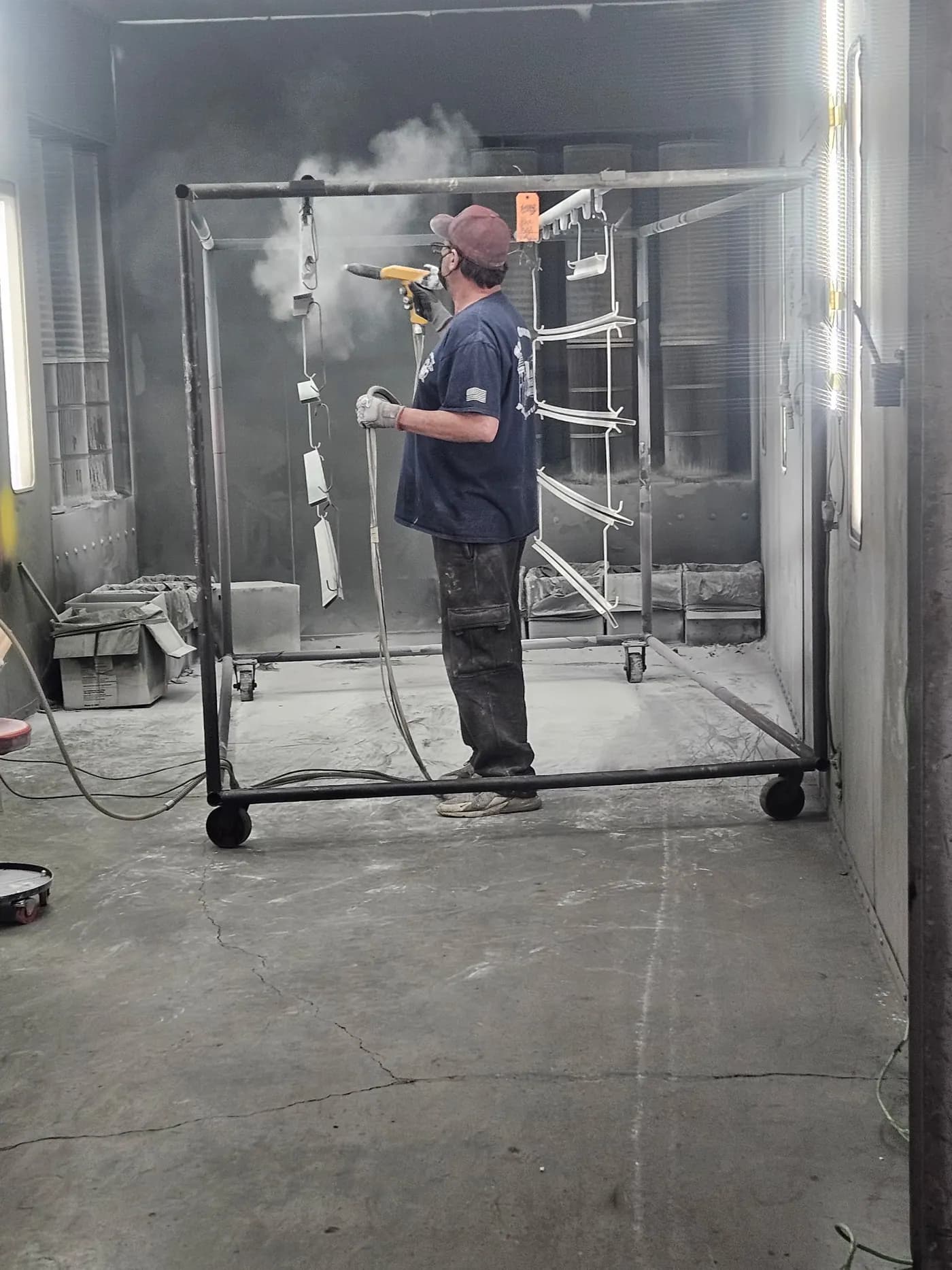 Technician applying powder coating to a metal frame on a rolling rack.
